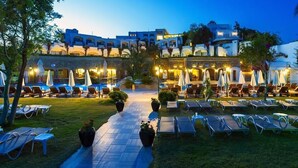 A hotel courtyard with sun loungers, umbrellas, and a pool area at dusk. - Royal Asarlik Beach Hotel & Spa - All Inclusive (Bodrum)