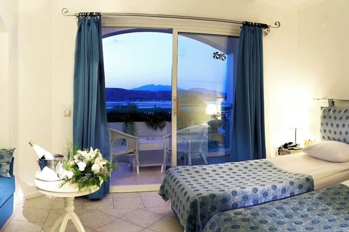 A hotel room with a balcony, a bed, a sofa, and a table with a flower arrangement.