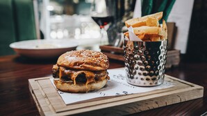 A burger and fries on a wooden board with a menu in the background. - The Wordsworth, Grasmere- The Inn Collection Group (Ambleside)