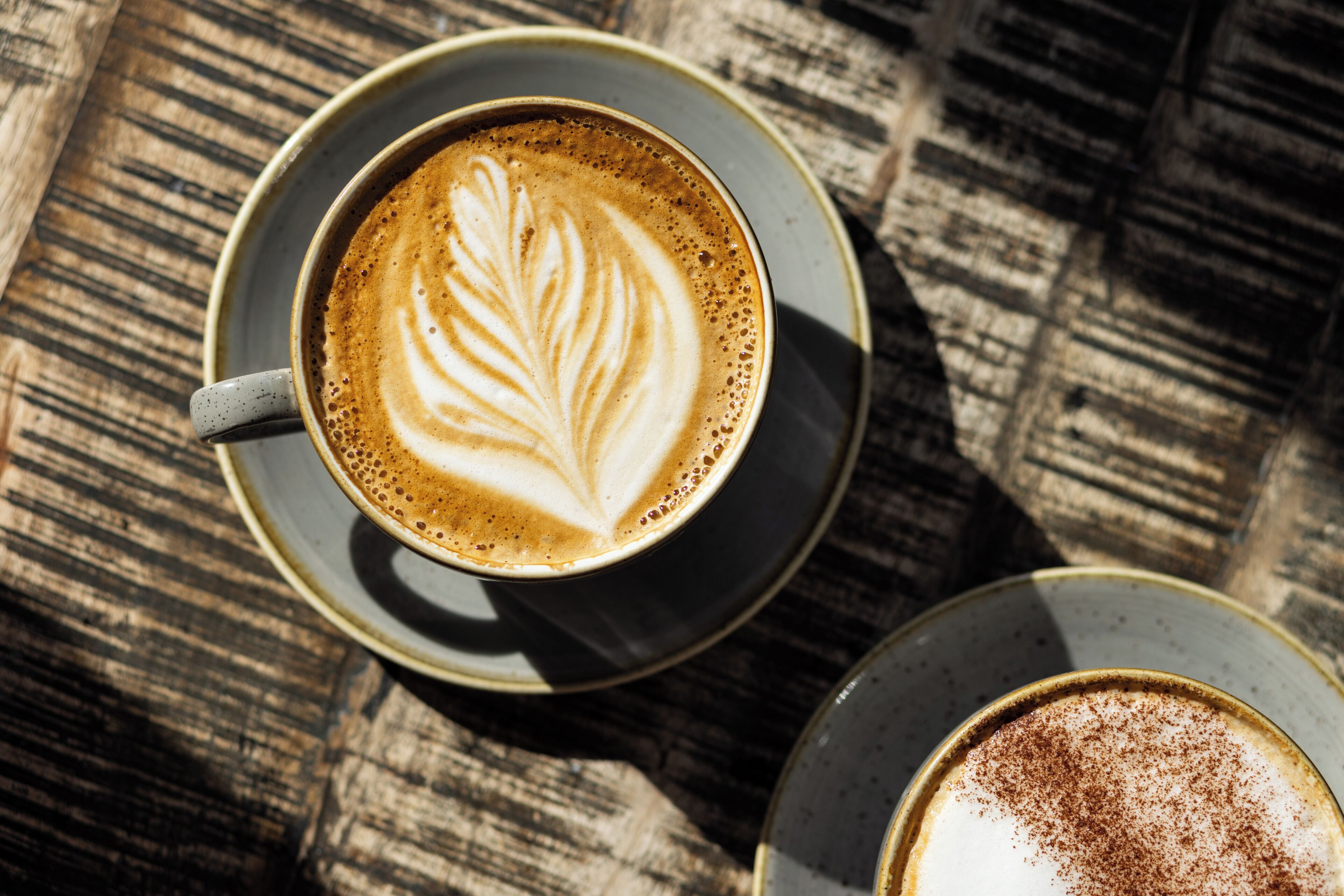 Une tasse de café ornée d’un motif en latte art, posée sur une table en bois.