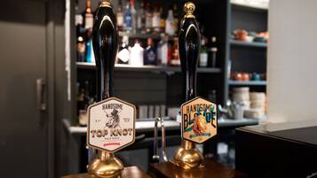 Two beer taps labeled 'HANDSOME' and 'TOP KNOT' with a bar in the background.
