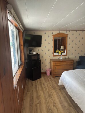 A bedroom with a wooden floor, a bed, a dresser, a television, and a window with blinds. - Starlight Inn (Bennington)