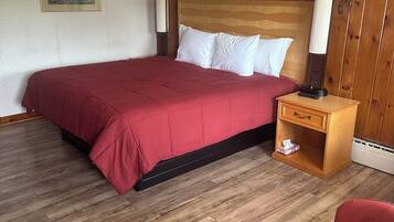 A hotel room with a wooden headboard, a red bedspread, two white pillows, a nightstand with a lamp, and a red chair.