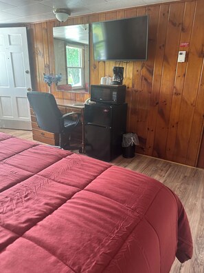 A room with a bed, a desk with a computer, a TV, and a microwave.