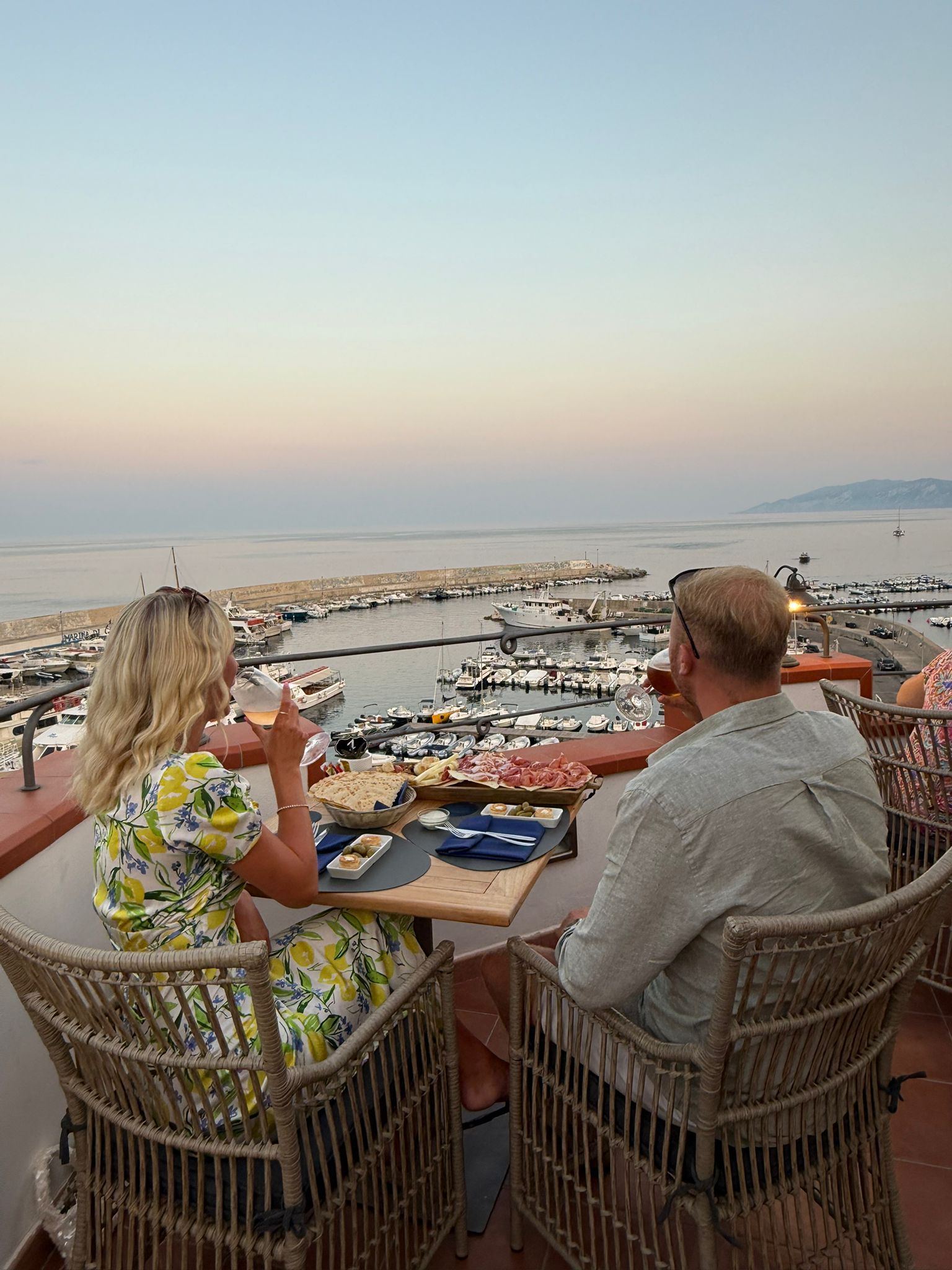 A couple dining at an outdoor table with a view of a marina and boats.