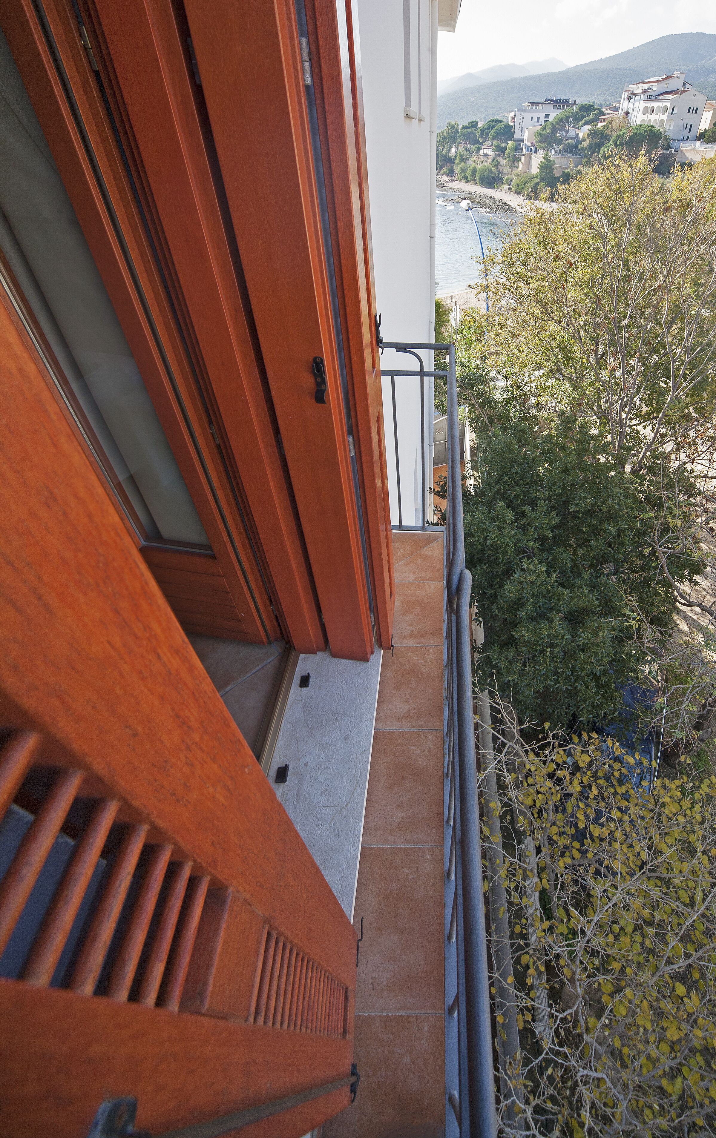 Un balcone in legno con ringhiera metallica che si affaccia su una zona costiera con edifici e vegetazione.