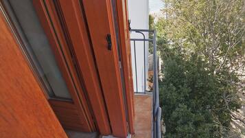 Un balcone in legno con ringhiera metallica che si affaccia su una zona costiera con edifici e vegetazione.