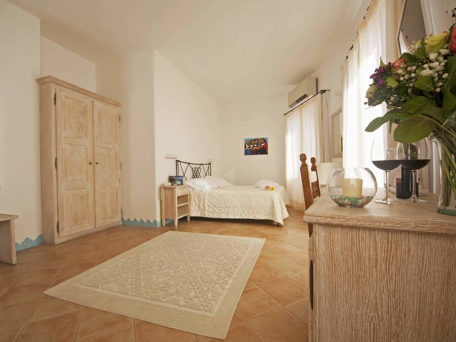 A bedroom with a bed, bedside table, lamp, and a decorative vase with flowers.