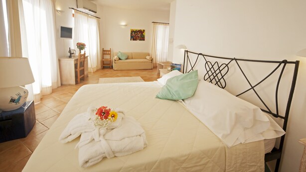 A hotel room with a bed, a desk, a chair, a sofa, and a TV. - BUE MARINO HOTEL & ROOFTOP BAR (Dorgali)
