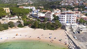 Una cittadina costiera con spiaggia sabbiosa, edifici con balconi e montagne sullo sfondo.