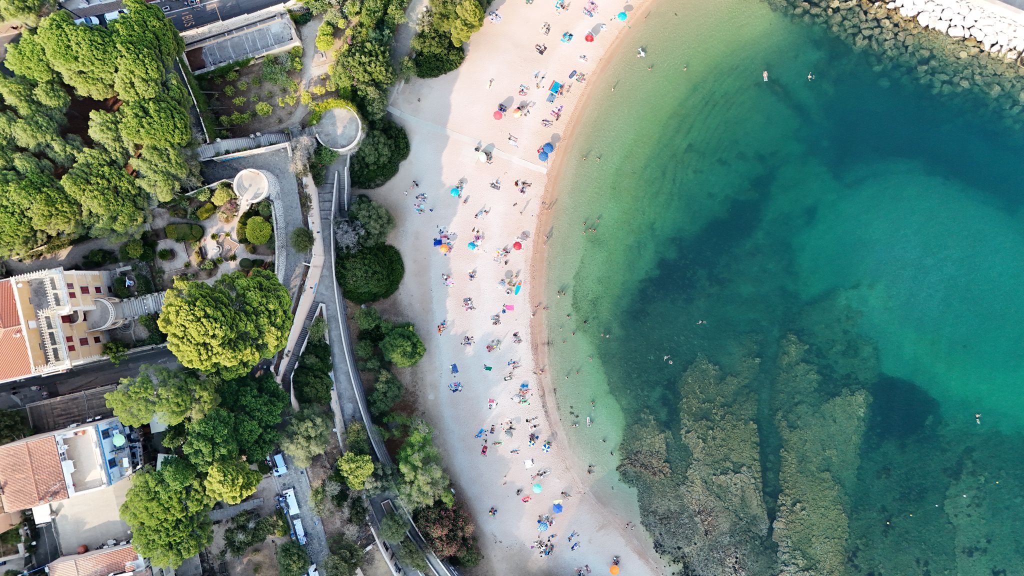 An aerial view of a beach with people, a clear water area, and surrounding greenery.