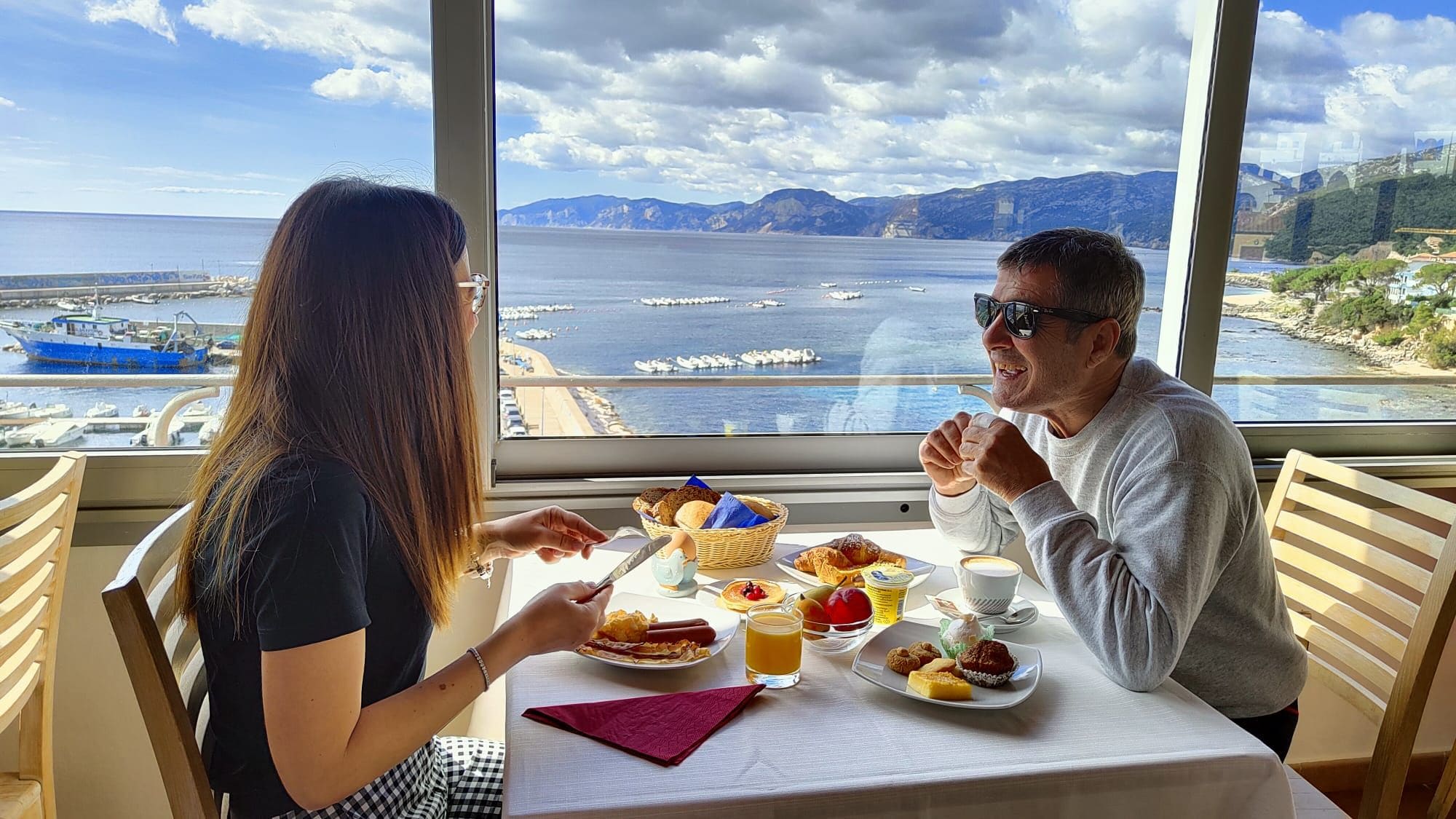 Ein Esstisch mit Frühstücksangeboten und Blick auf das Meer und Boote.