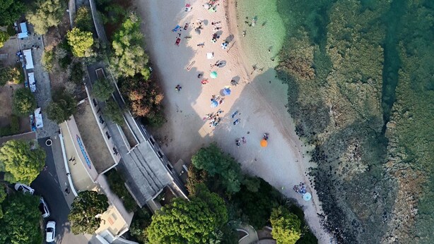 An aerial view of a beach with clear water, surrounded by greenery and a road with vehicles. - BUE MARINO HOTEL & ROOFTOP BAR (Dorgali)