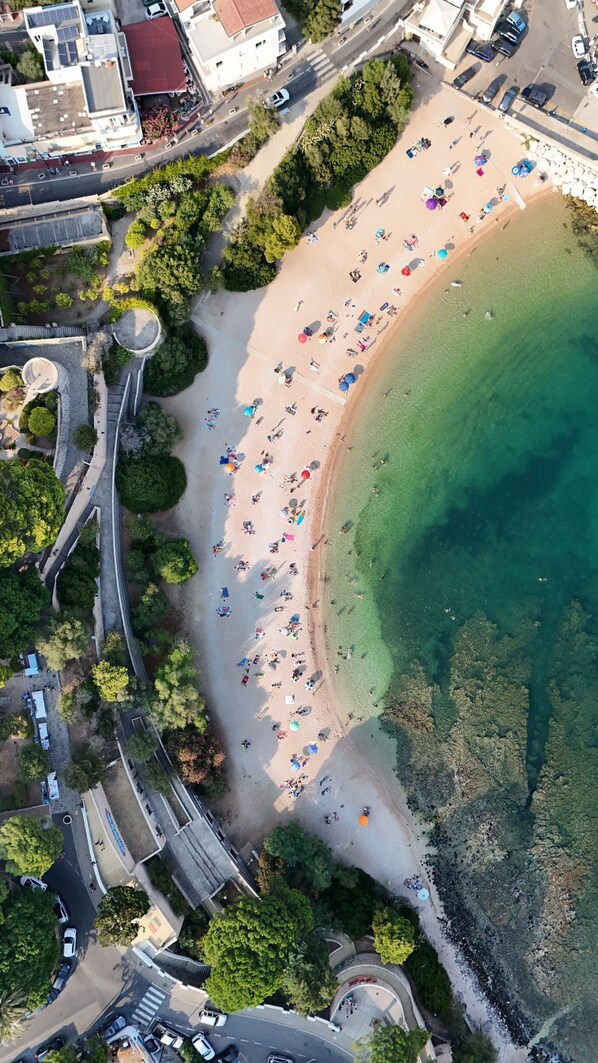 Vista aérea de una playa con agua cristalina, rodeada de vegetación y una carretera con vehículos.