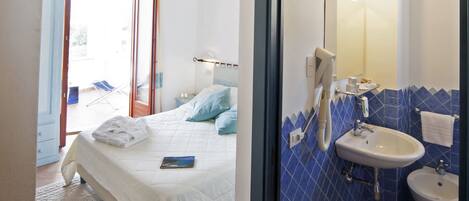 A hotel room with a bed, a bathroom with a sink and mirror, and a view of the outside.