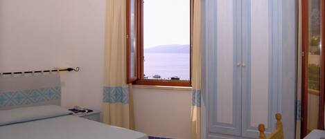 Un dormitorio con cama, armario, mesita de noche, teléfono y ventana con vistas al mar.