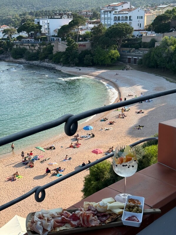 A balcony with a view of a beach, a glass of drink, and a platter of food. - BUE MARINO HOTEL & ROOFTOP BAR (Dorgali)