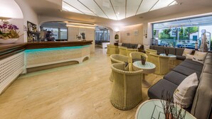 A modern hotel lobby with a reception desk, seating area, and large windows offering a view of the outdoors. - Hotel Diamond (Riccione)