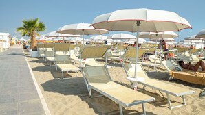 A beach with rows of sun loungers under white umbrellas, a palm tree, and a clear sky. - Hotel Diamond (Riccione)