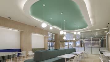 A modern waiting area with a curved green ceiling, seating arrangements, and a glass wall offering a view of the interior.