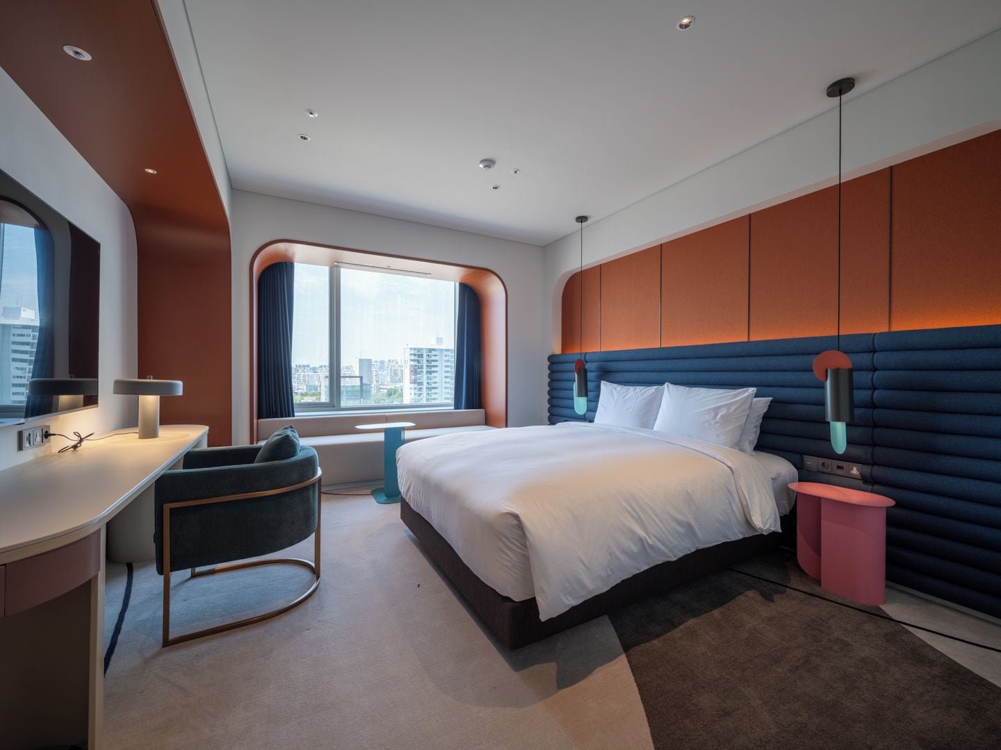 A modern hotel room with a large bed, a desk, and a view of the city.