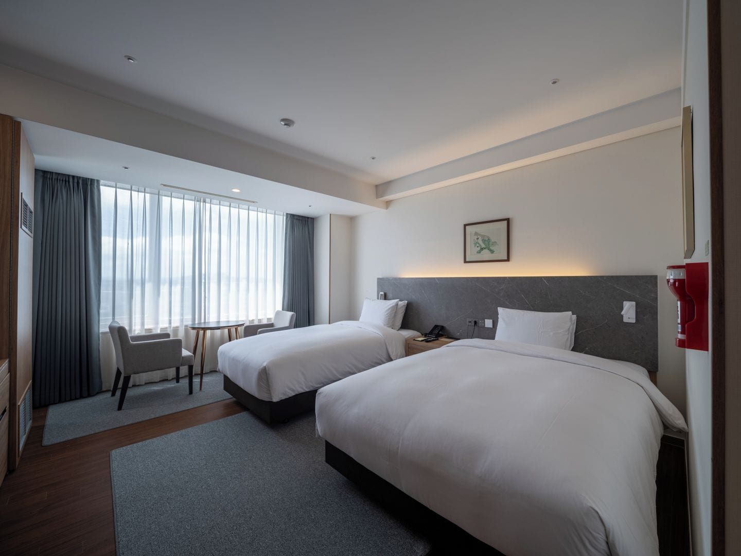 A hotel room with two beds, a desk, and a chair.
