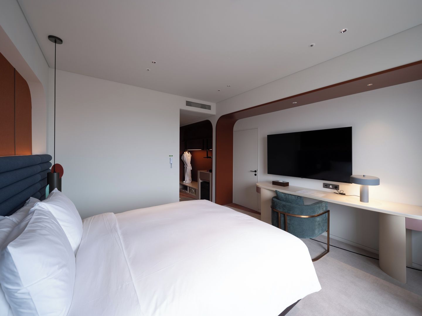 A modern hotel room with a large bed, a desk, a flat-screen TV, and a separate bathroom area.