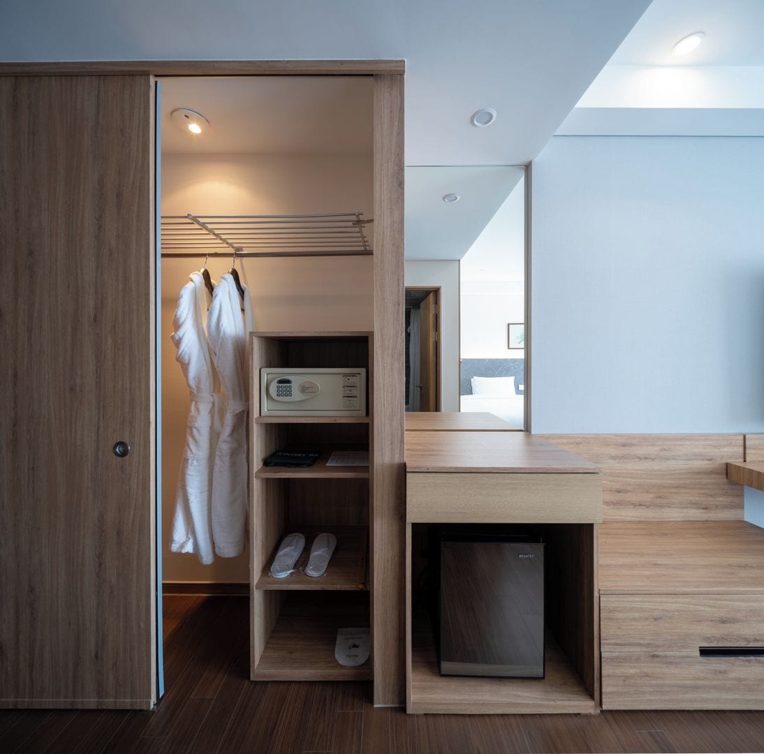 A modern hotel room with a walk-in closet, a wooden desk, and a built-in shoe storage.