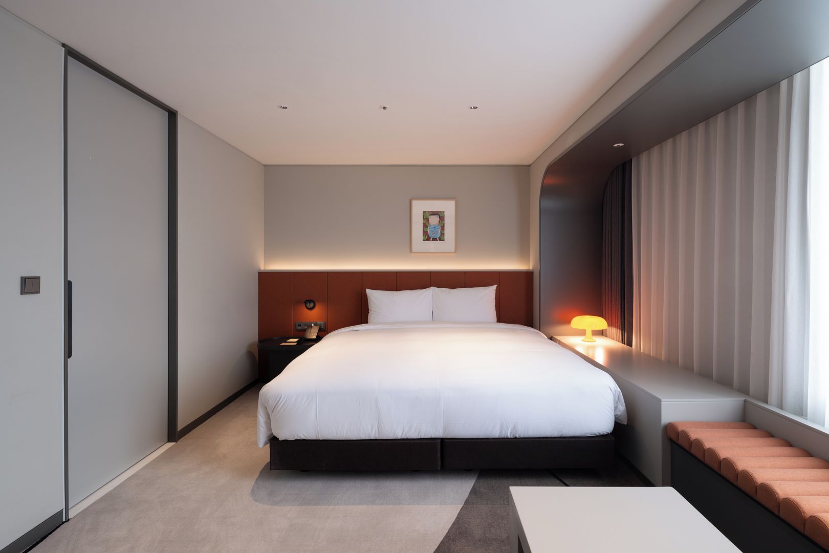 Una habitación de hotel moderna con una cama grande, mesita de noche, lámpara y una ventana con cortinas.