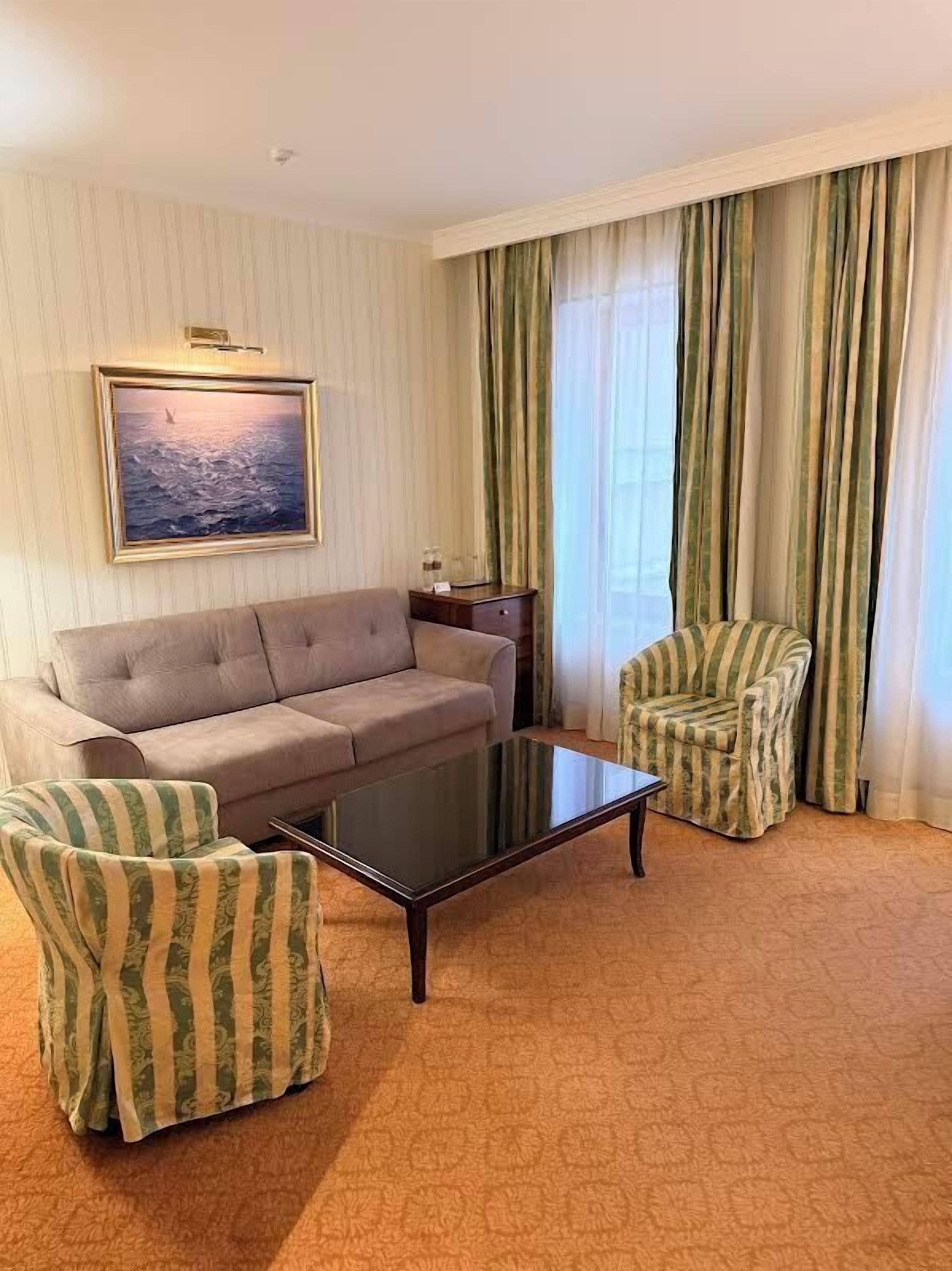 Habitación de hotel con sofá, sillón a rayas y una mesa de centro de cristal.