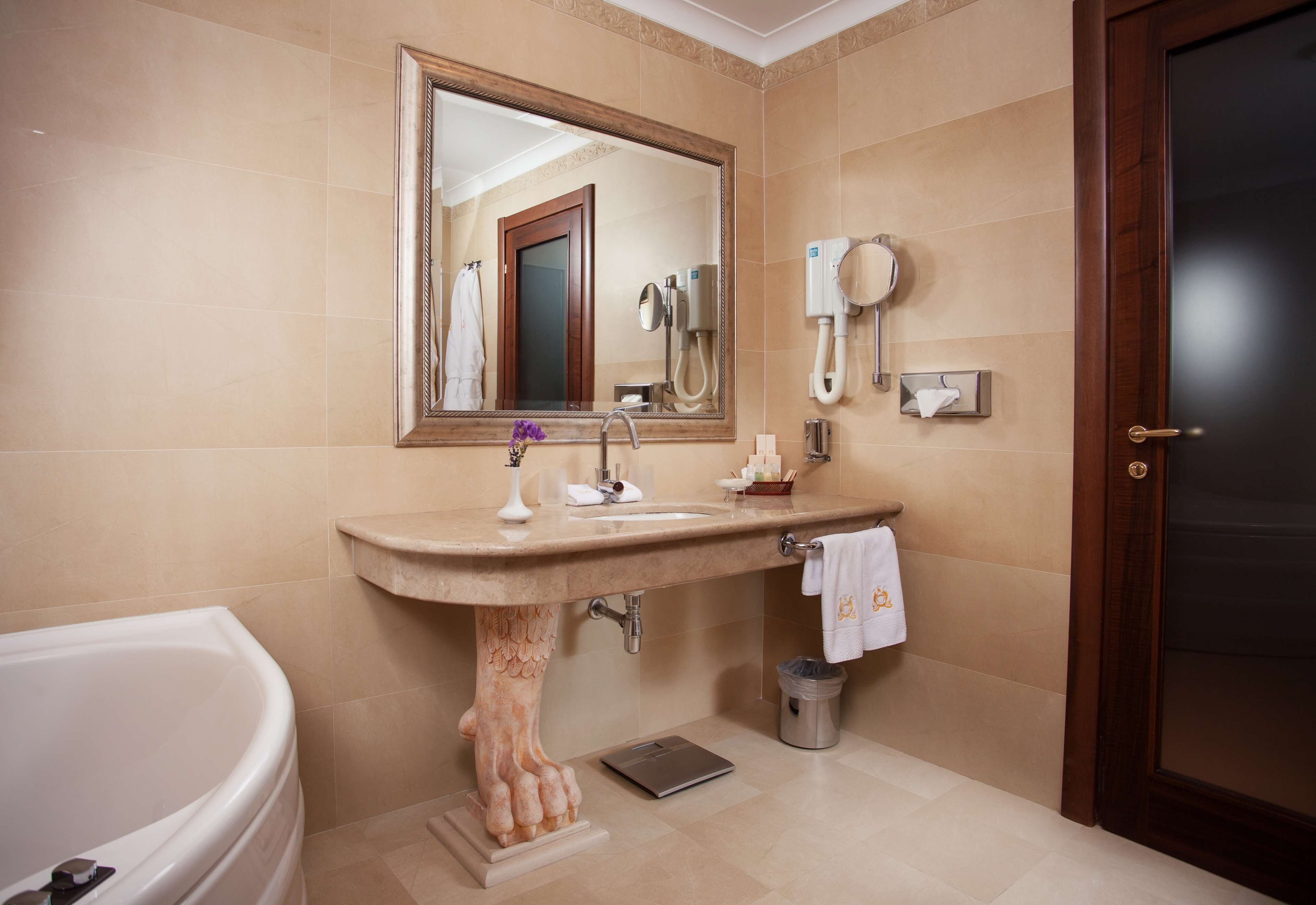Une salle de bain avec un grand miroir, un lavabo, un porte-serviettes, un sèche-cheveux et une poubelle.