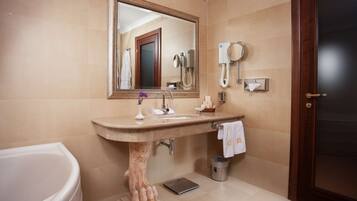 Une salle de bain avec un grand miroir, un lavabo, un porte-serviettes, un sèche-cheveux et une poubelle.