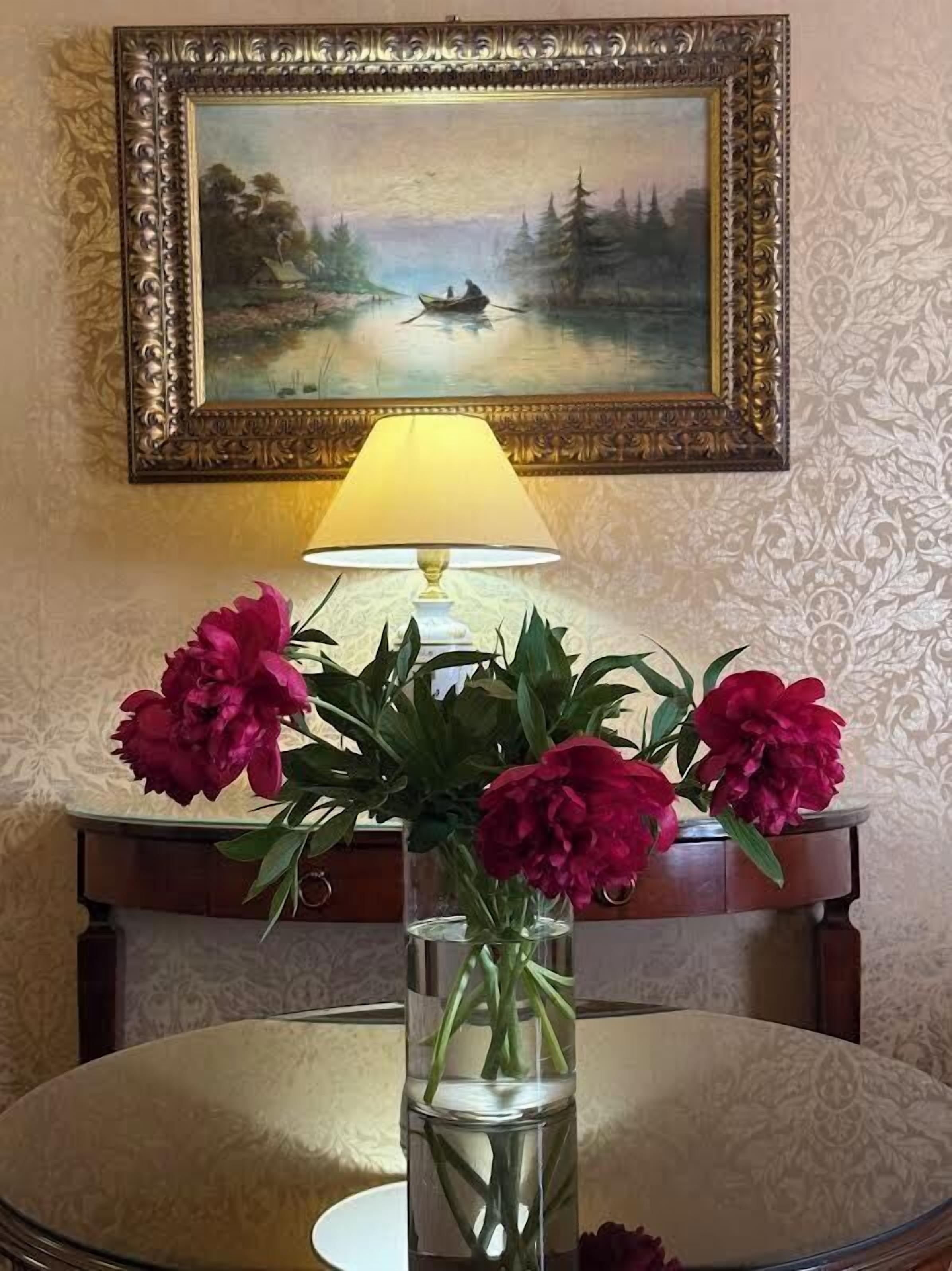 Una mesa con un jarrón de flores, una lámpara y un cuadro en la pared.
