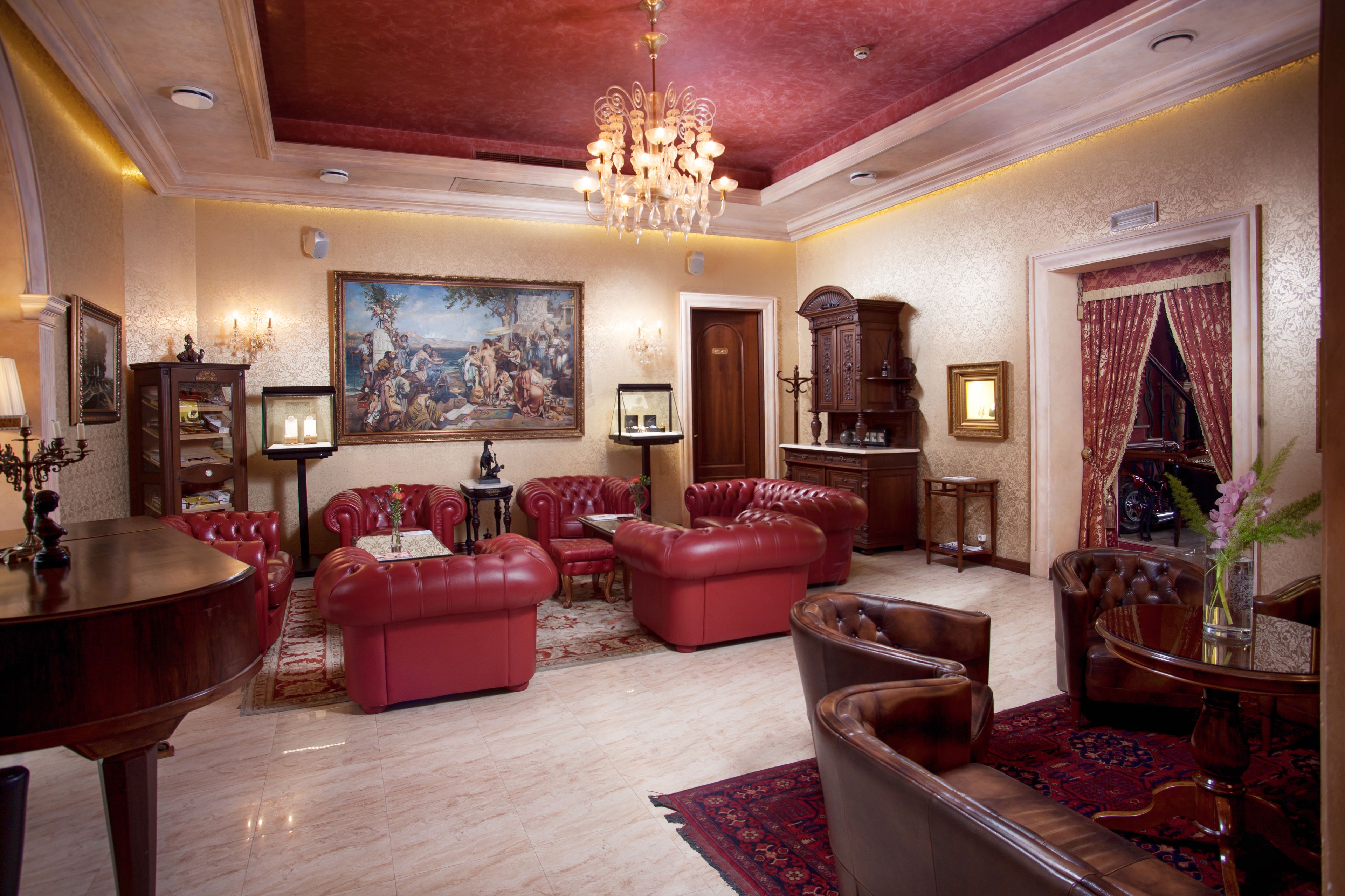 Uma sala de estar espaçosa com sofás de couro vermelho, um lustre imponente e uma grande pintura clássica na parede.