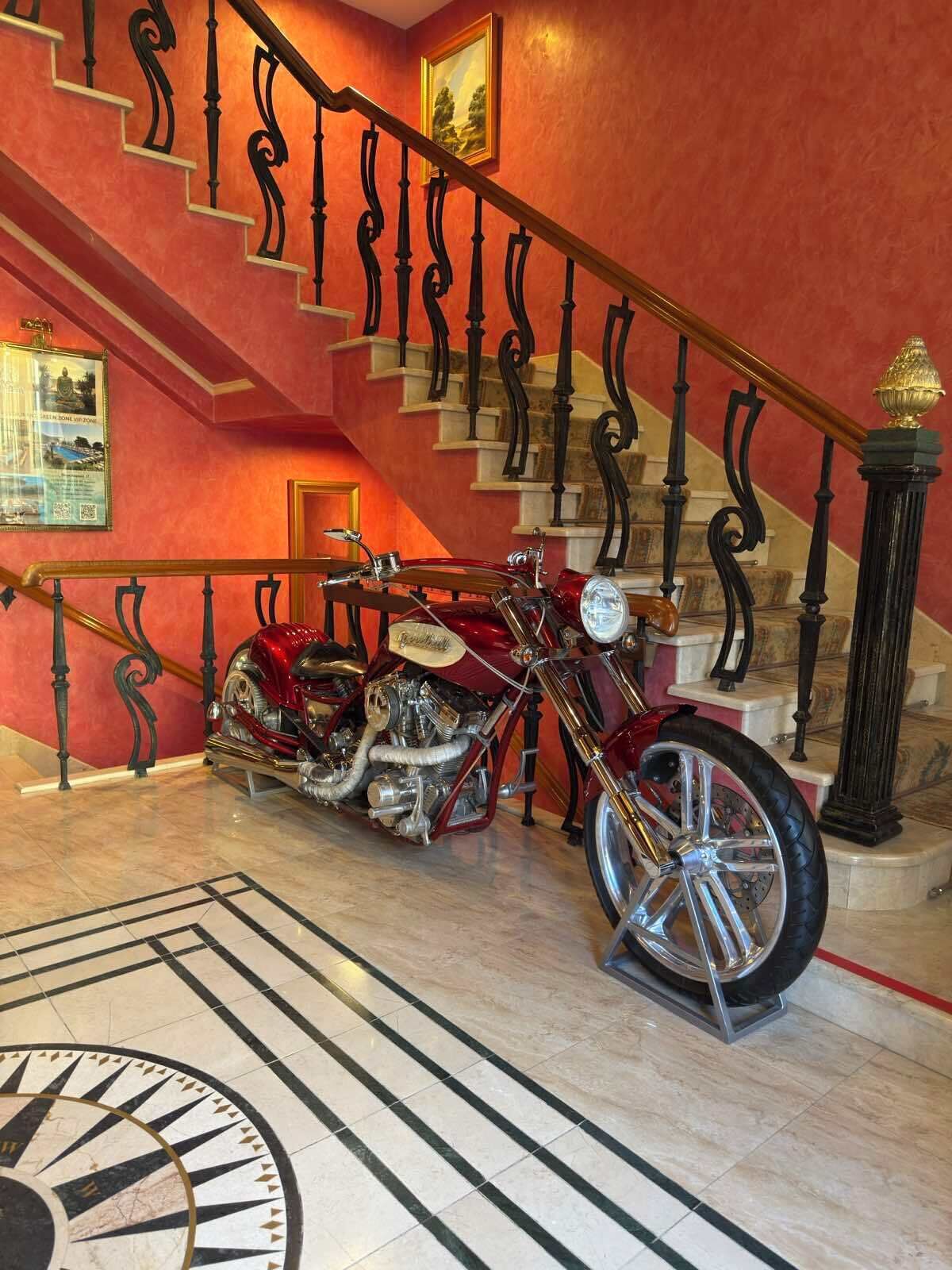 Een rode trap met gedetailleerde zwarte leuningen, een klassieke motorfiets en een groot rond vloerontwerp.