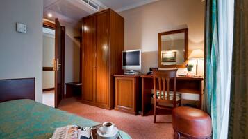 Une chambre d’hôtel avec un lit, un bureau avec un ordinateur, une chaise, une armoire et une petite table sur laquelle se trouvent une tasse de café et un journal.