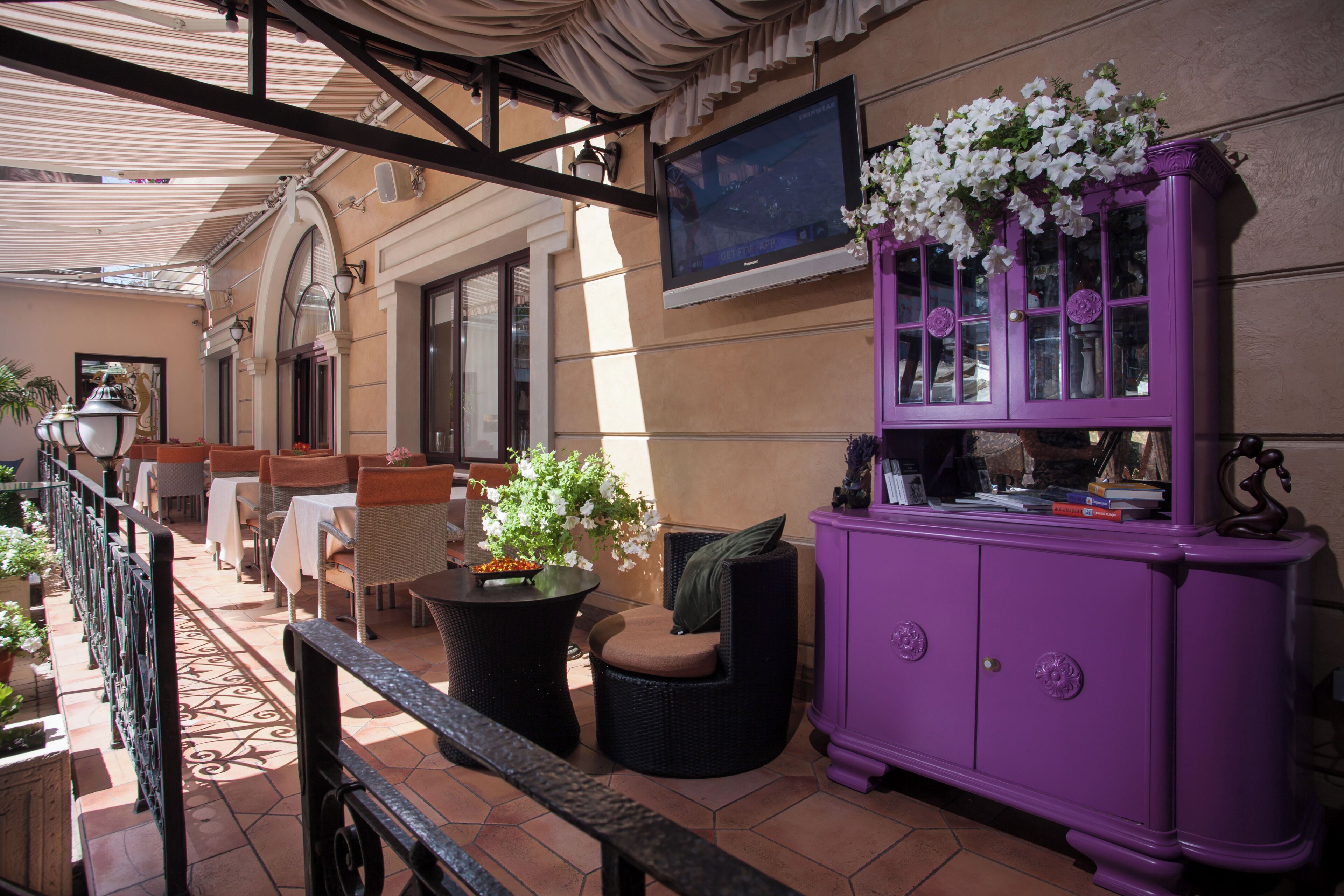 Eine Terrasse mit Sitzgelegenheit im Freien, einem violetten Schrank und einem an der Wand befestigten Fernseher.