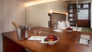 A hotel room with a wooden table set with a champagne bottle, two wine glasses, and a bowl of fruit. - Hotel Otrada (Odesa)