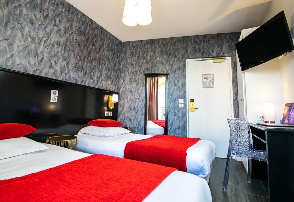 A hotel room with two beds, a desk, a chair, a TV, and a door.