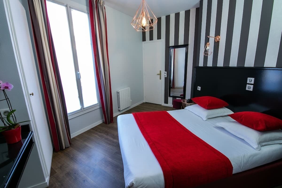 Une chambre d’hôtel avec un lit, un miroir, un radiateur et une fenêtre avec des rideaux.