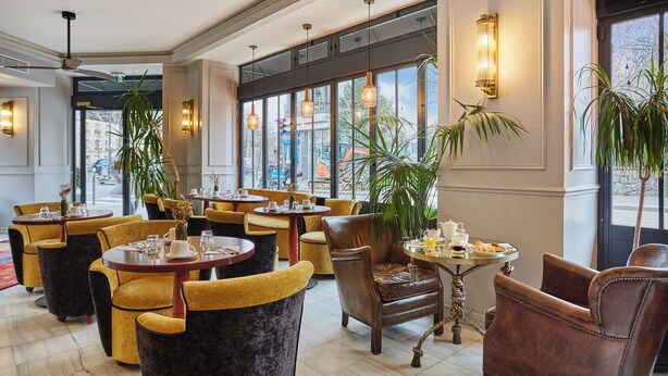 A hotel lobby with round tables, yellow and brown chairs, large windows, and hanging pendant lights. - Eiffel Villa Garibaldi (Paris)