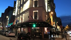 A multi-story hotel with illuminated signage, a prominent entrance, and a flag display. - Eiffel Villa Garibaldi (Paris)