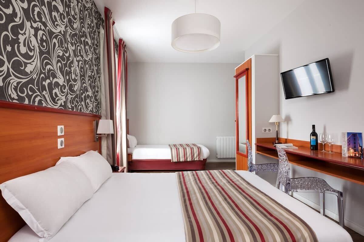 Une chambre d’hôtel avec un lit, un bureau, une télévision et un mur décoré de motifs.
