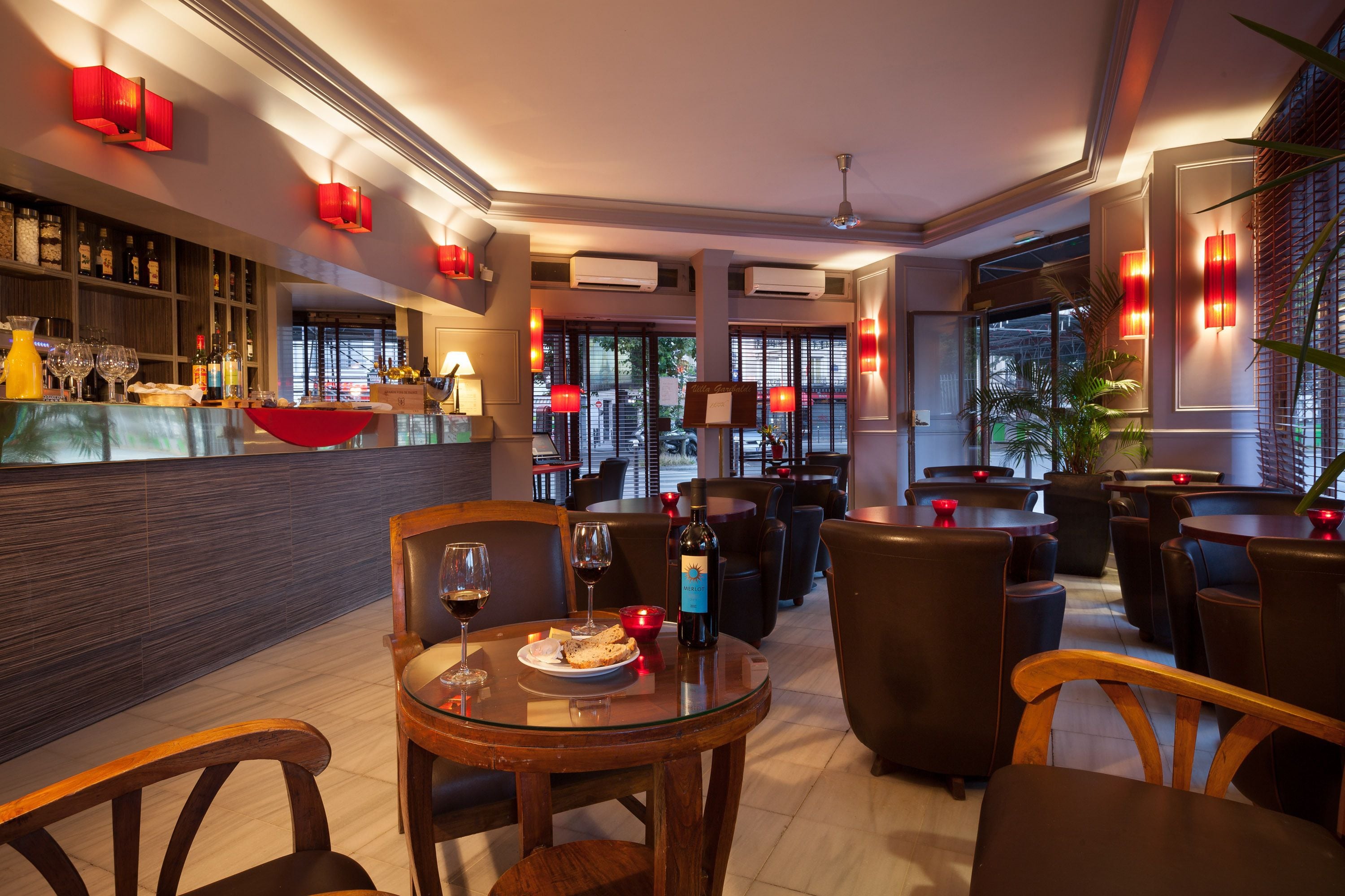 En restaurant med barområde, runde borde og stole. Der er røde lanterner og et stort vindue i baggrunden.
