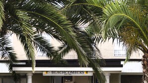 Entrada de un hotel con un letrero que dice 'BEACHCOMBERS', rodeada de palmeras y parterres de flores.