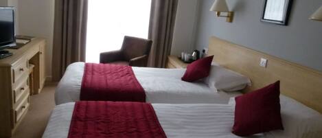Habitación de hotel con dos camas, televisión, una silla y una lámpara.