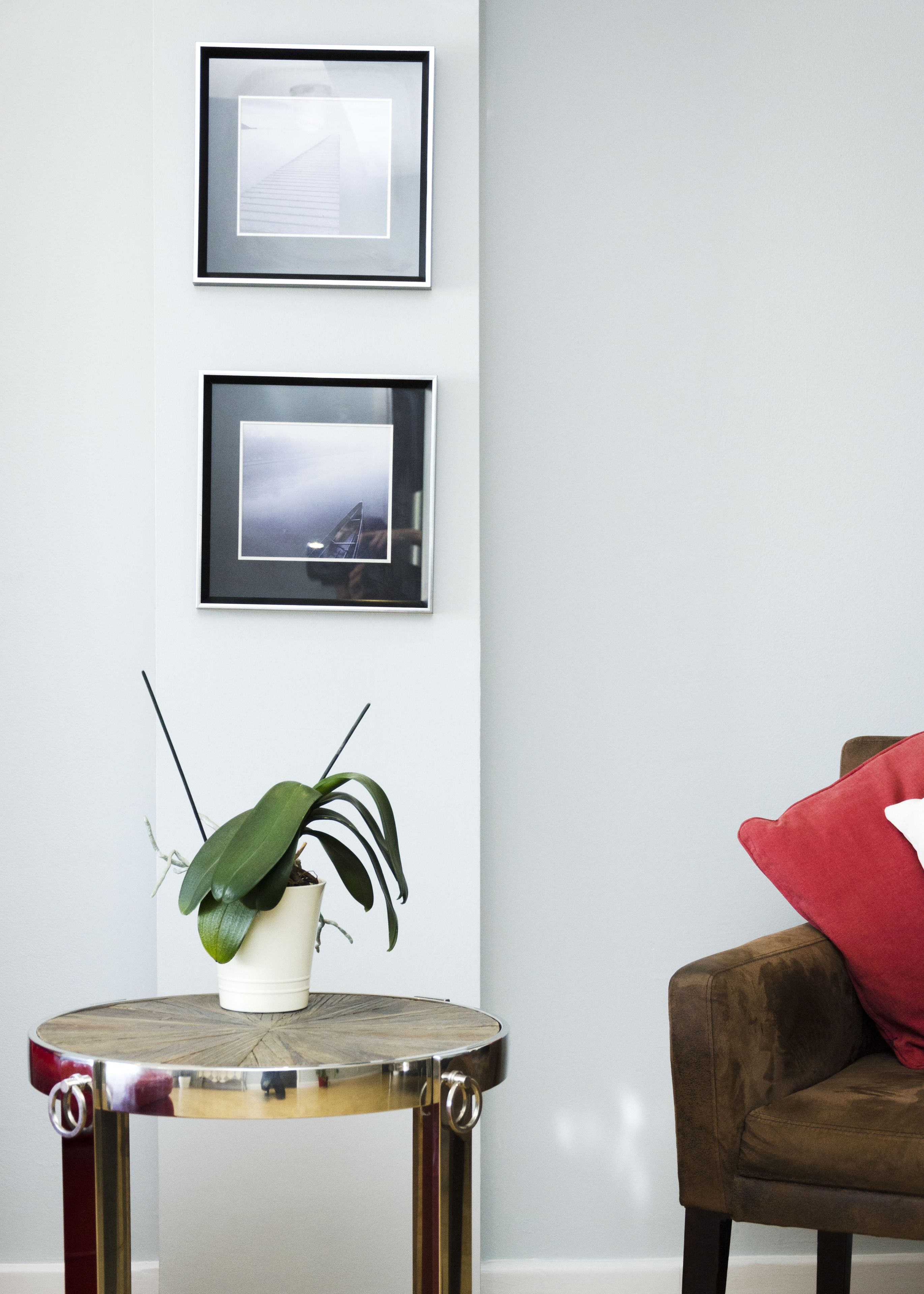 Um quarto com uma mesa redonda, um vaso de planta, uma cadeira marrom e duas imagens emolduradas na parede.