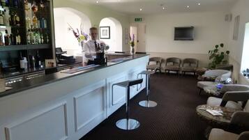 A bar area with a bartender, a seating area with chairs and a sofa, and a television mounted on the wall.