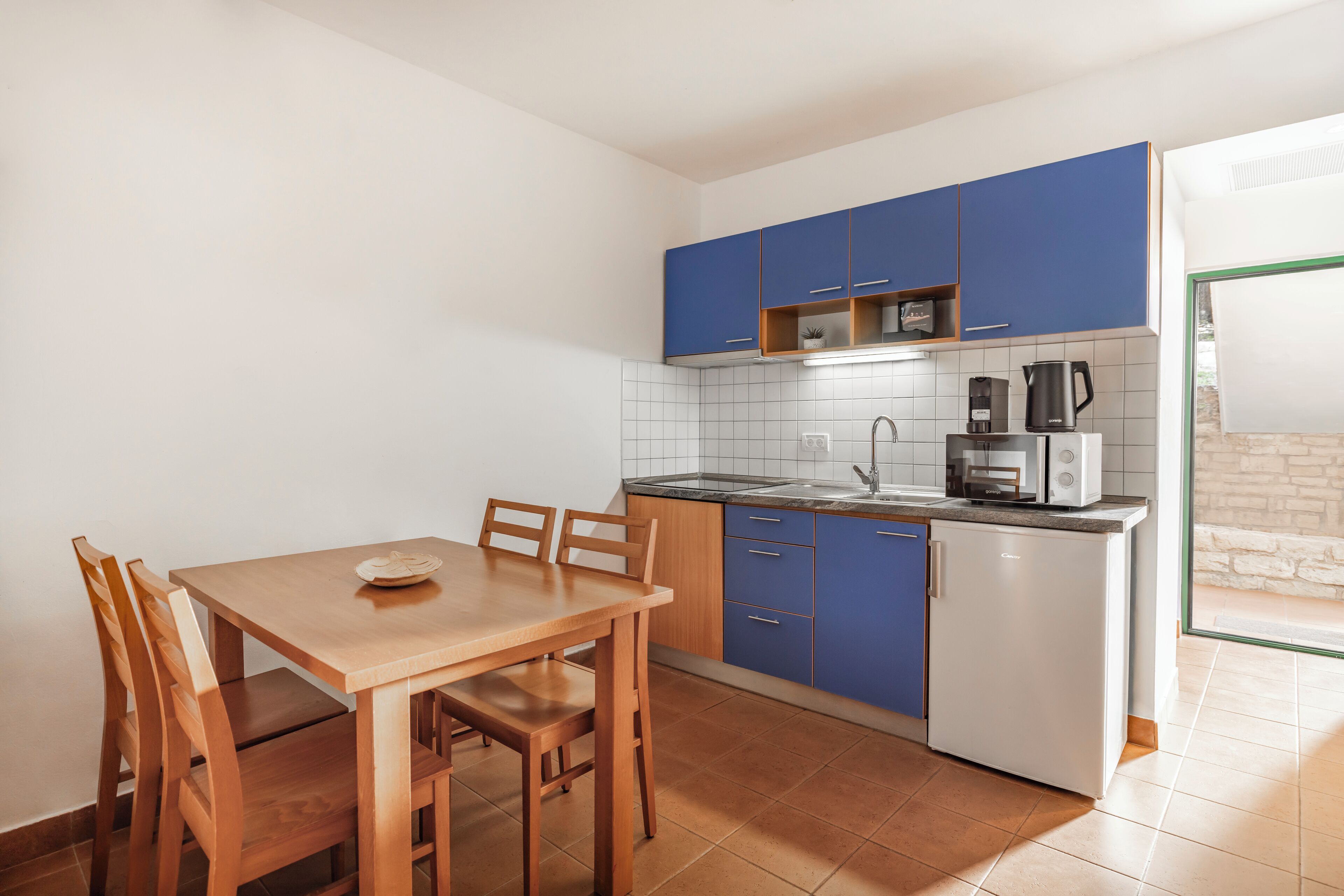 A compact kitchen with blue cabinets, a white refrigerator, and a dining table with chairs.
