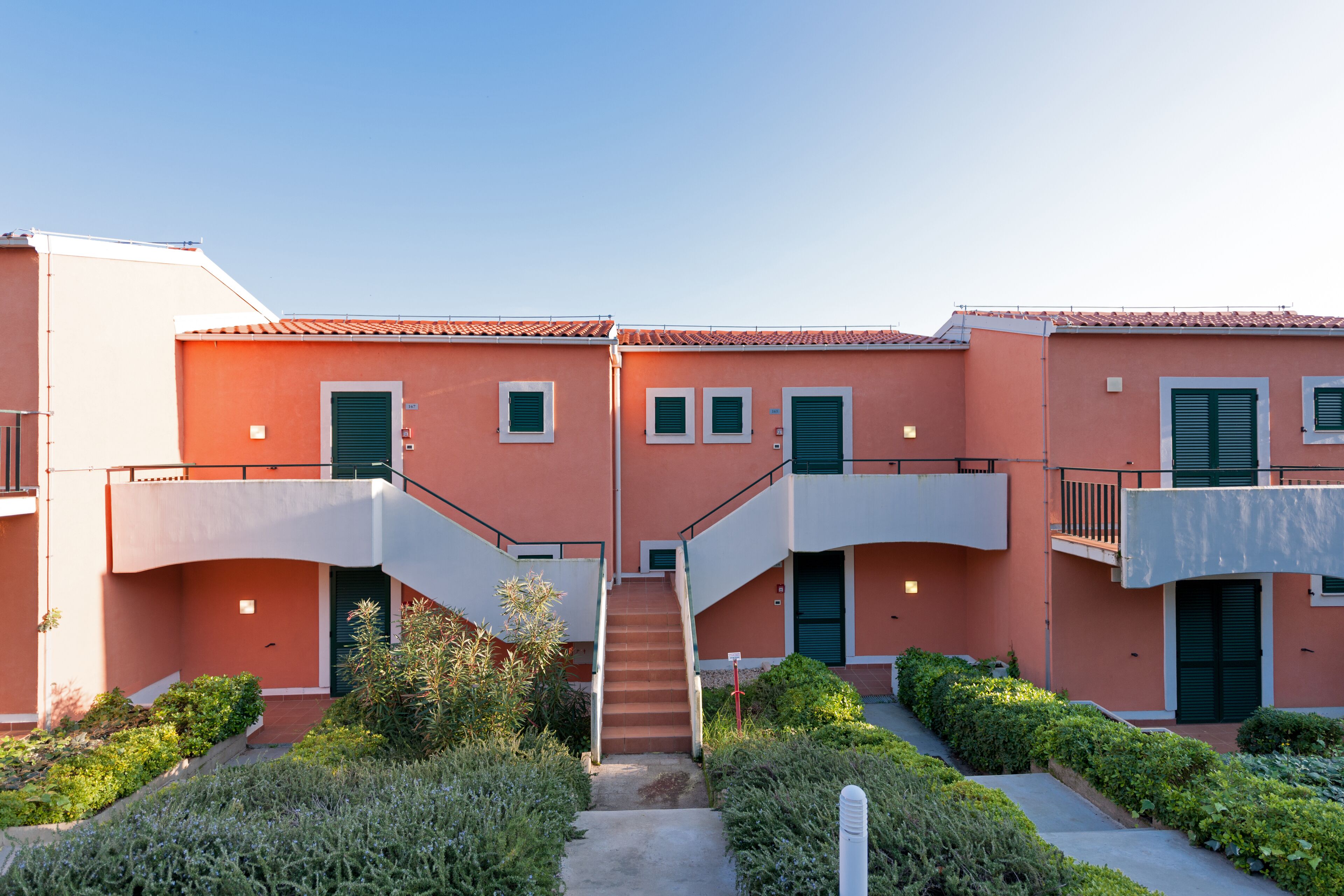 A building with a central staircase, multiple balconies, and a garden area.